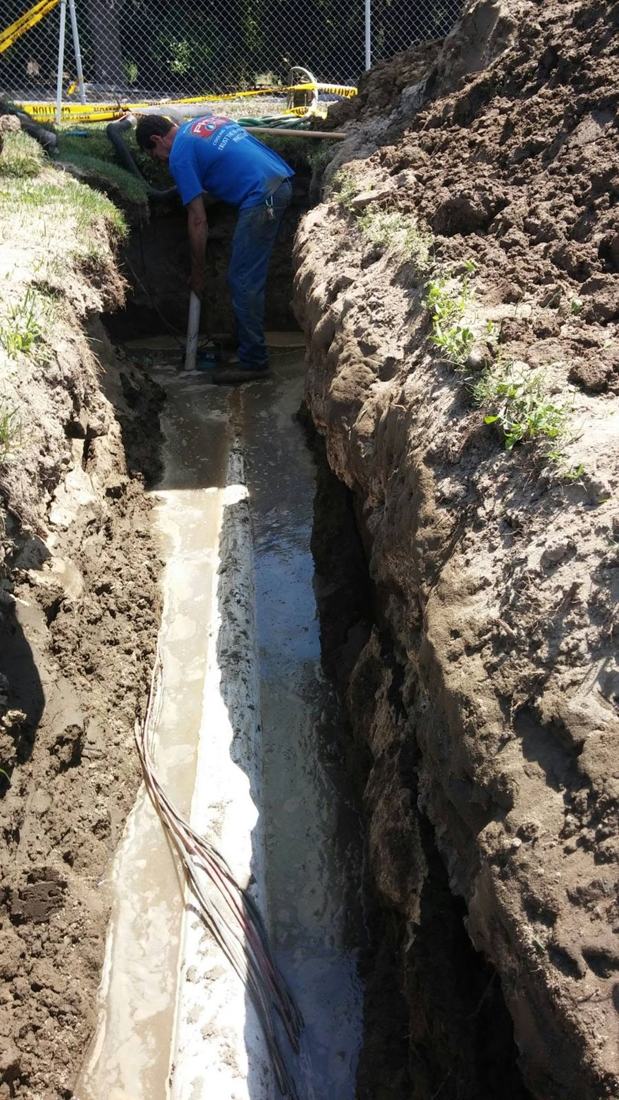Plumber working in a deep excavated trench to repair an underground pipe